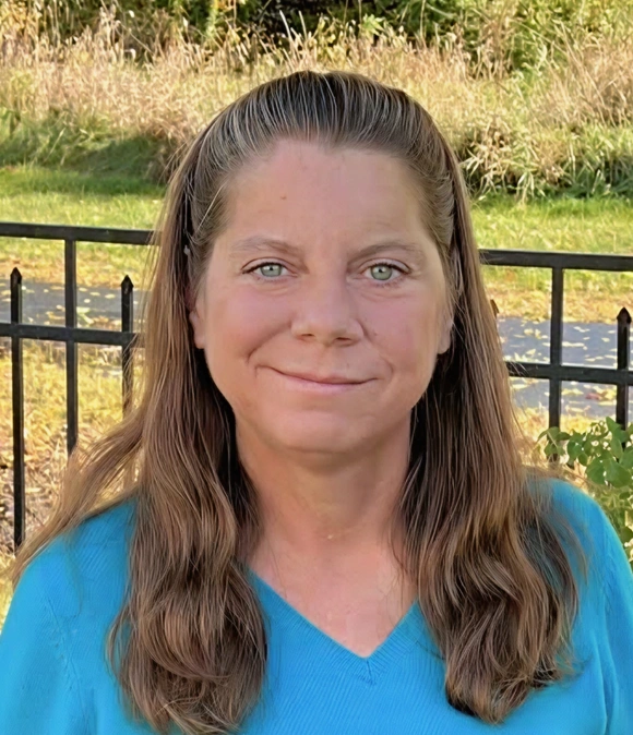 Outdoor portrait of Dr. Jennifer smiling in a teal top with a fenced field in the background
