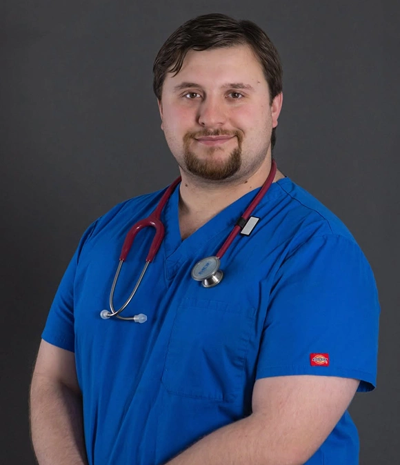 Portrait of Dr. Kenneth, a veterinarian, smiling in blue scrubs with a stethoscope around his neck